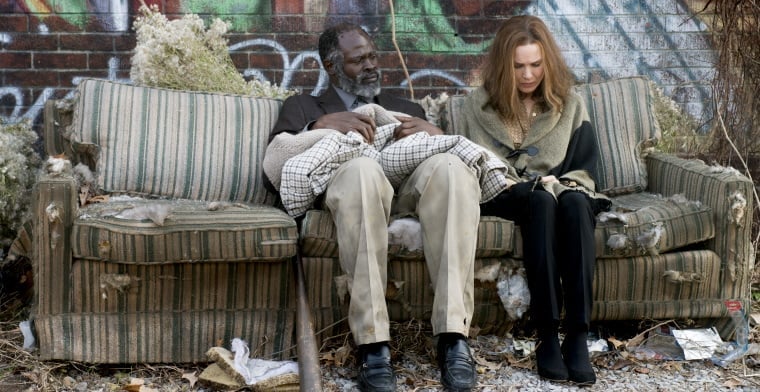 A film still of Denver and Debbie sitting on a dirty couch on the street surrounded by trash